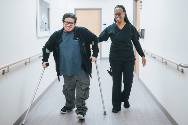 A Rehabilitation patient smiling while walking with crutches
